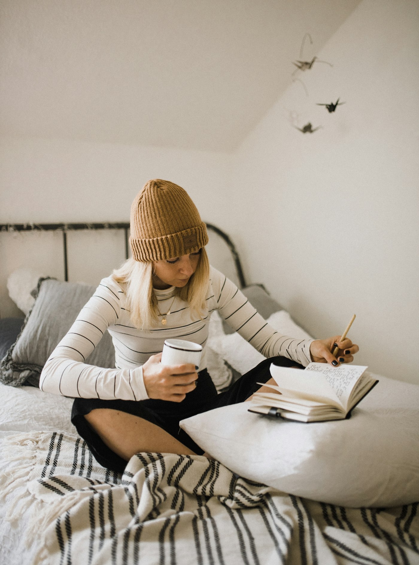 Woman in striped shirt sitting on bed while writing