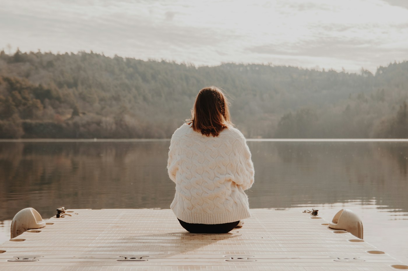 Woman in white long sleeve shirt sitting on brown wooden dock during daytime