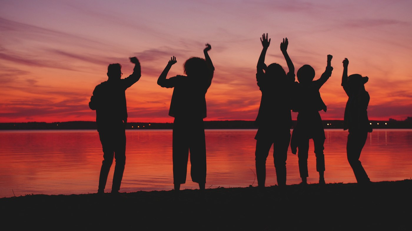 Silhouettes of people dancing by the water at sunset