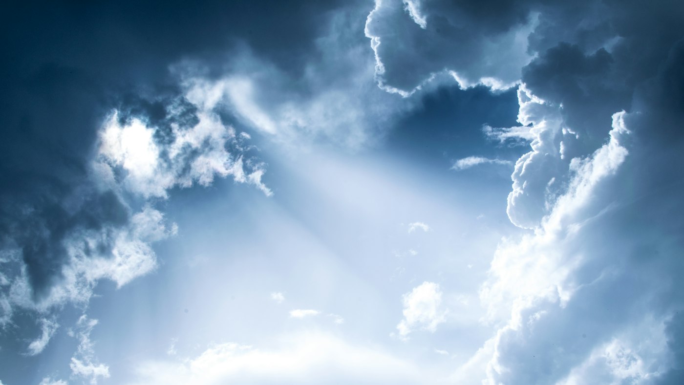 Bright light filtering through dense blue clouds in a vast sky